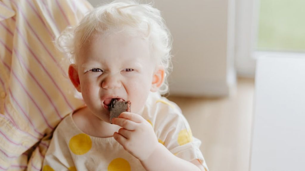 A cute albino child enjoying a chocolate snack indoors. Warm and playful vibe.